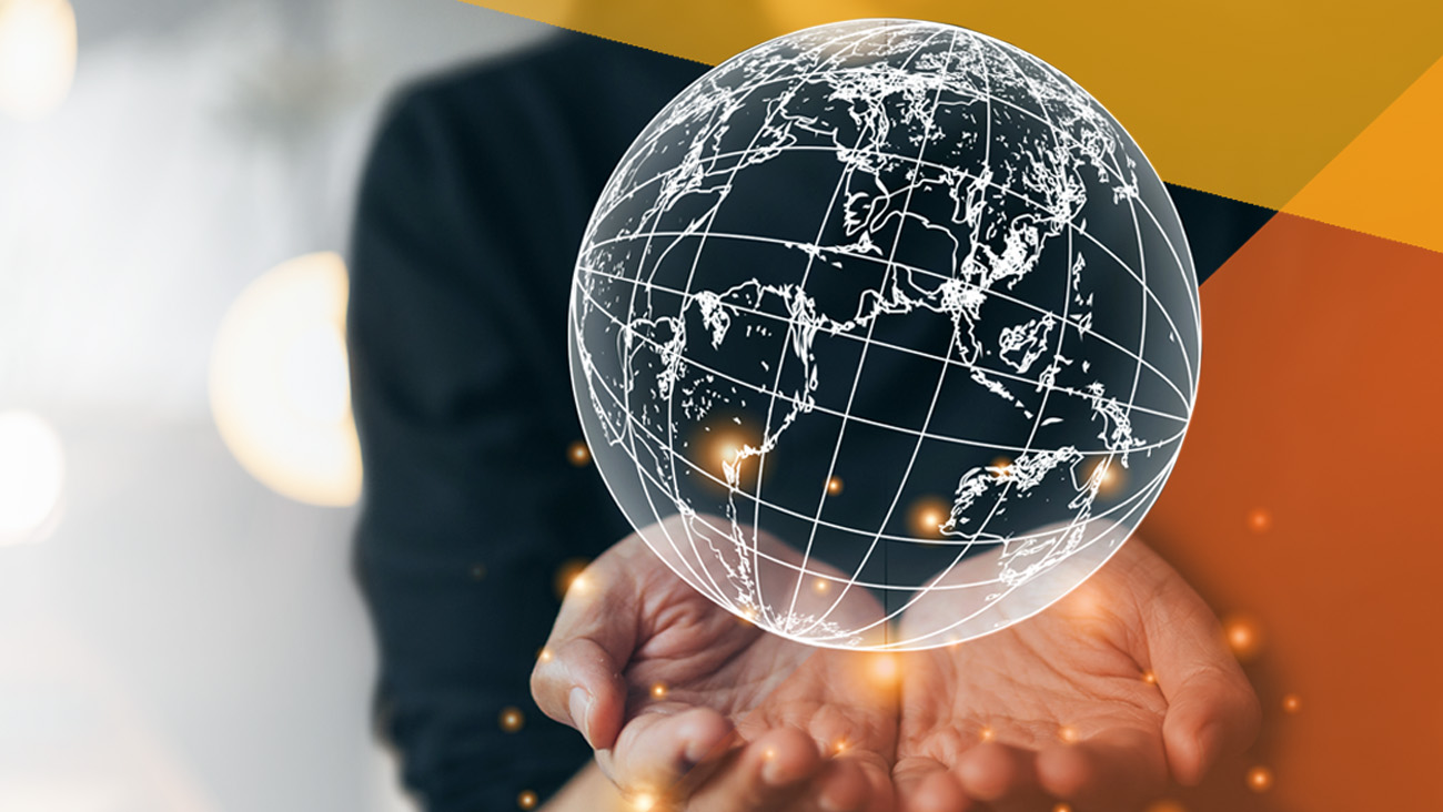 A person holds out their hands with a digital, translucent globe floating above them, illuminated by small glowing points. The globe displays continents and grid lines. The background is blurred, with abstract geometric shapes in the top corner.