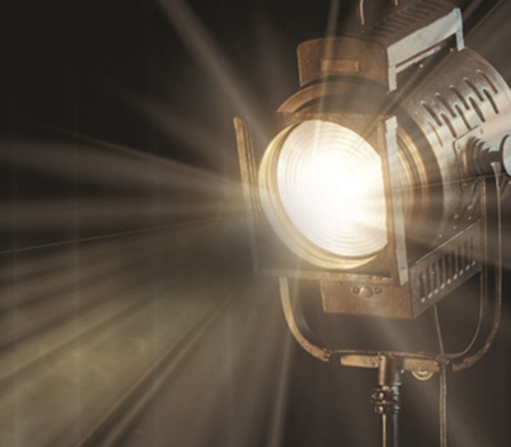 A vintage studio spotlight, reminiscent of a data-transforming channel, emits a bright, focused beam of light that creates intricate rays against a dark background. Mounted on a metal stand, its intense glow highlights the textured surface of the spotlights casing.