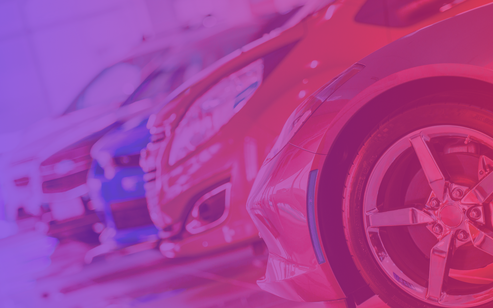 Close-up of several parked cars in a row inside a showroom, with a color overlay of pink and blue hues giving the image a vibrant, abstract effect.