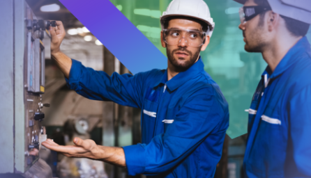 Two workers in blue uniforms and hard hats operate machinery in a factory.