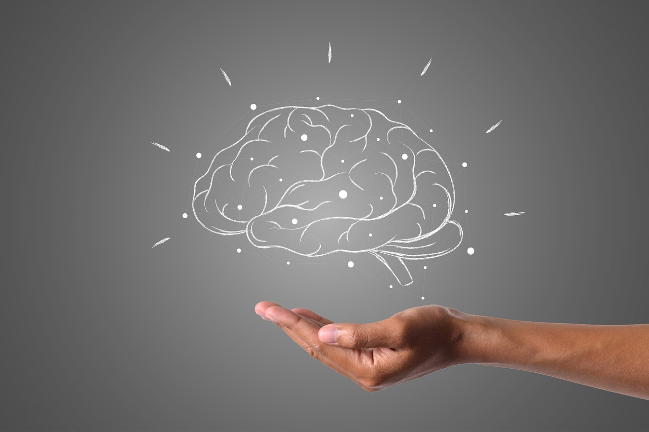 A hand extending upward with a digitally illustrated brain hovering above it. The brain is outlined in white on a gray background, with small lines emanating from it, suggesting ideas or creativity.