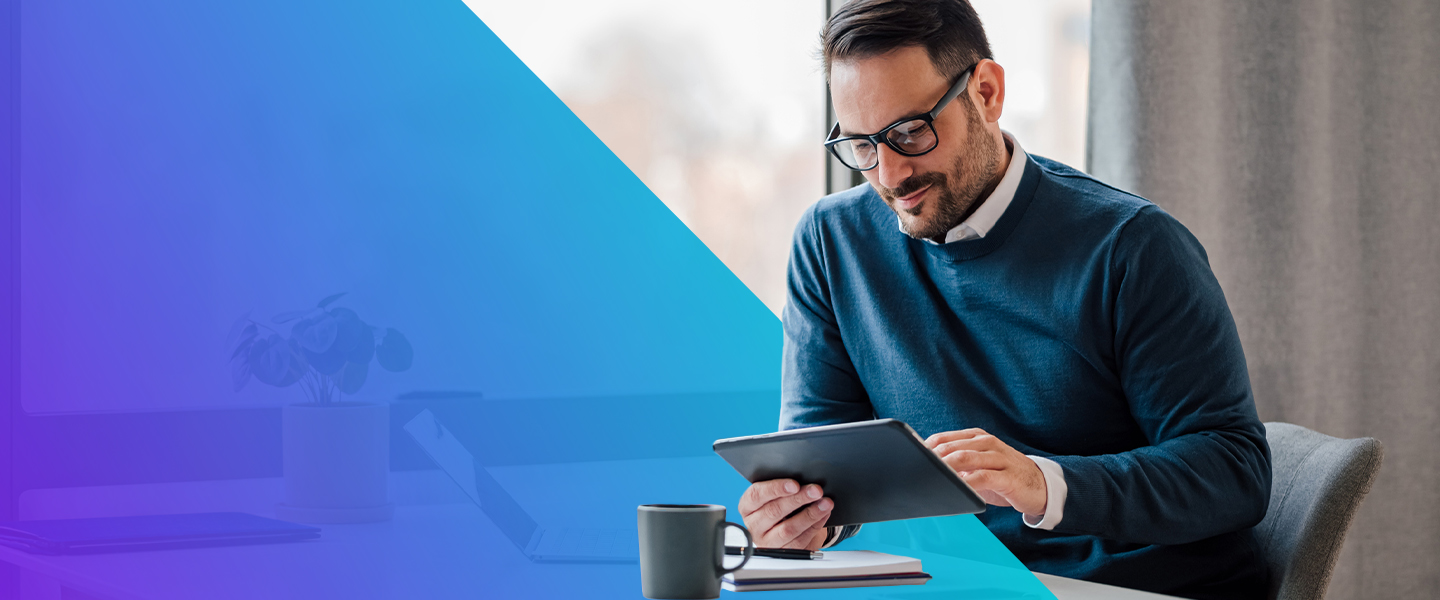 A man with glasses sits at a desk, using a tablet. A notebook, pen, and coffee mug are on the table. The background is bright with a large window and a gradient blue overlay covers part of the image.
