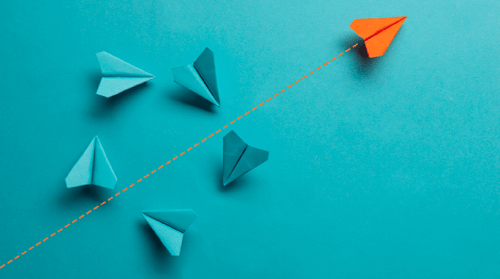 Six paper airplanes on a blue background, with five blue planes grouped together and one orange plane flying separately ahead on a dotted line, symbolizing leadership or standing out.