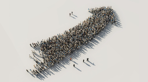 A large group of people standing together forms the shape of an upward-pointing arrow on a white background, casting long shadows.