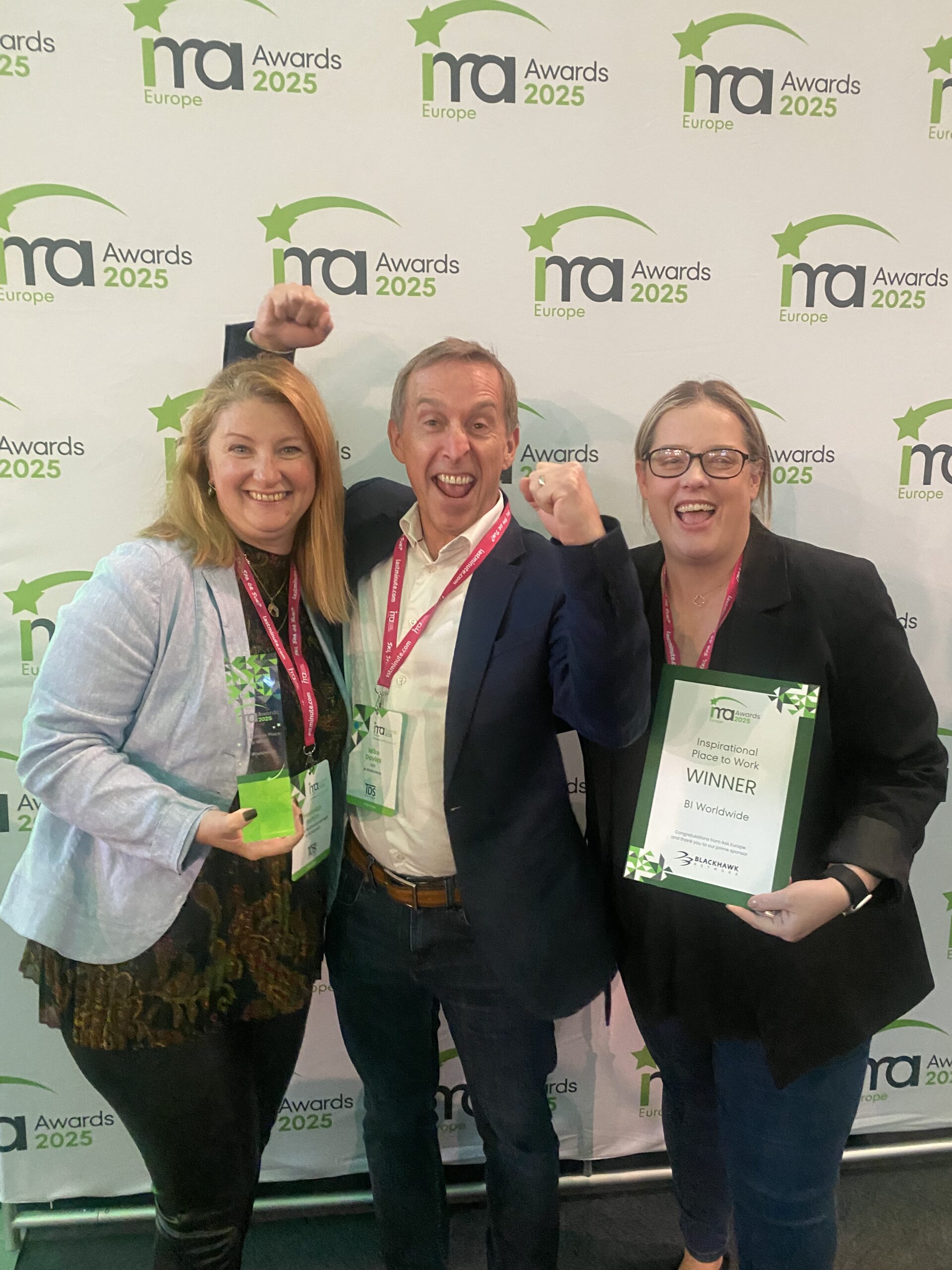 Three people smiling and celebrating at an awards event. One woman holds a trophy, another holds a framed certificate labeled Winner. Event backdrop reads ma Awards 2025 Europe.