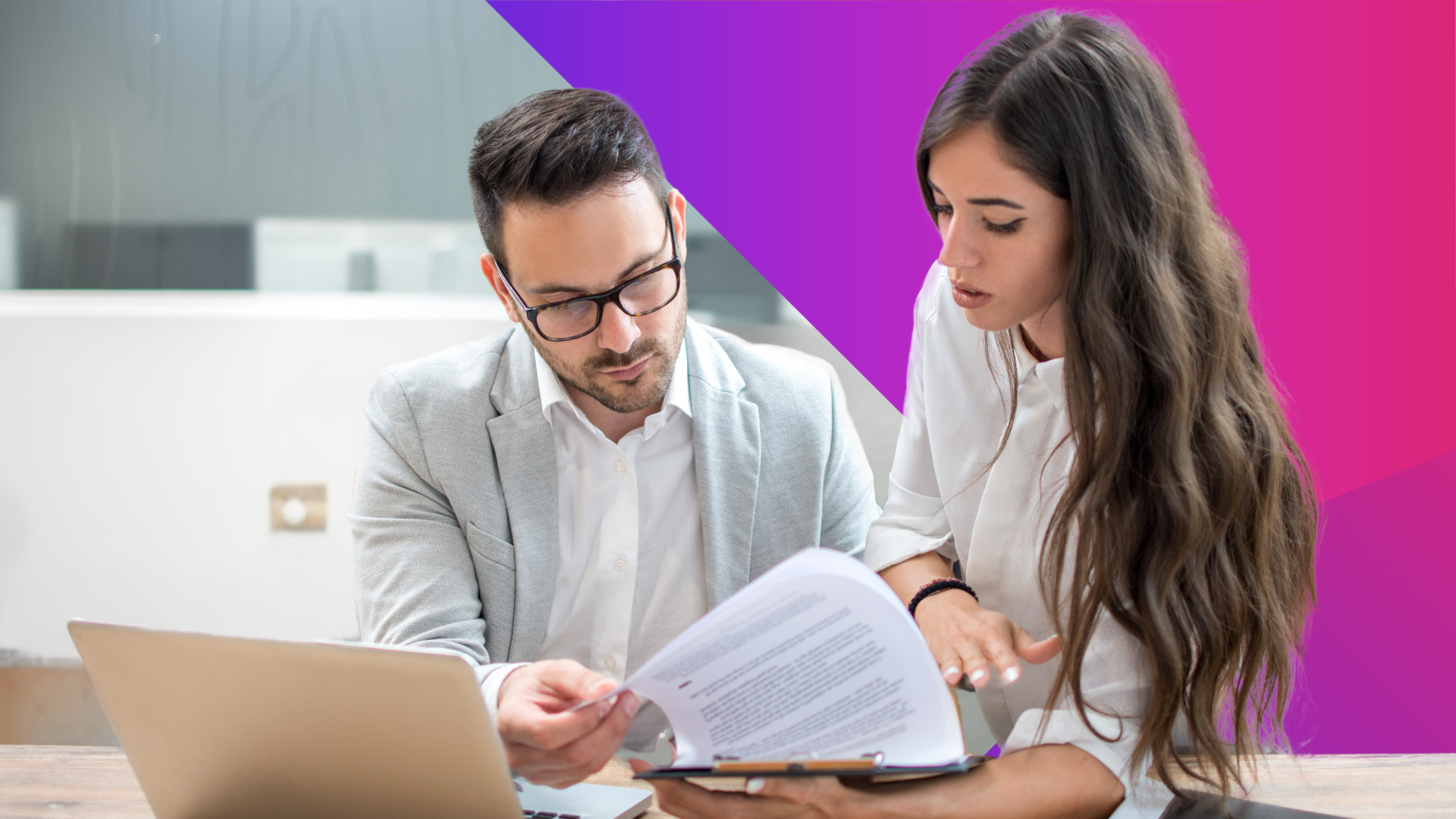A man in glasses and a light blazer and a woman with long brown hair in a white shirt review documents together at a desk with a laptop; a colorful geometric background is behind them.
