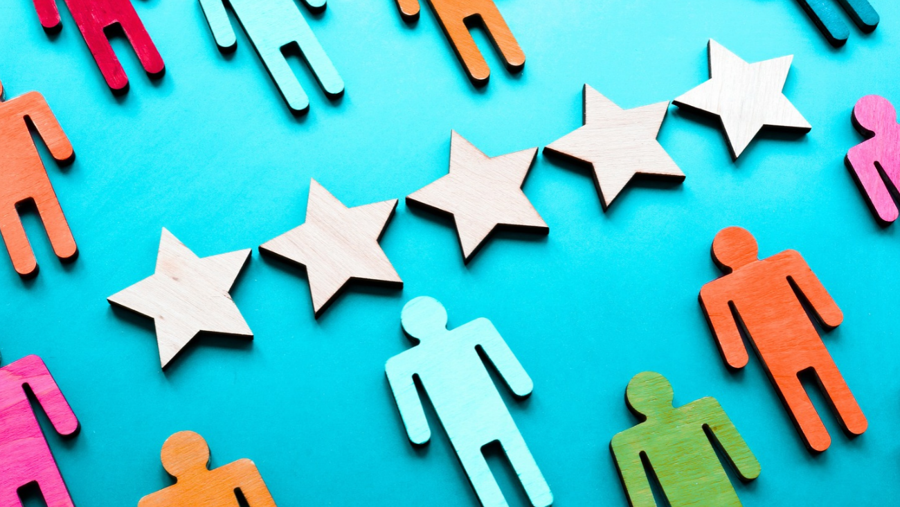 Colourful wooden human figures surround a row of five wooden stars on a bright blue background, representing evaluation, teamwork, or rating.