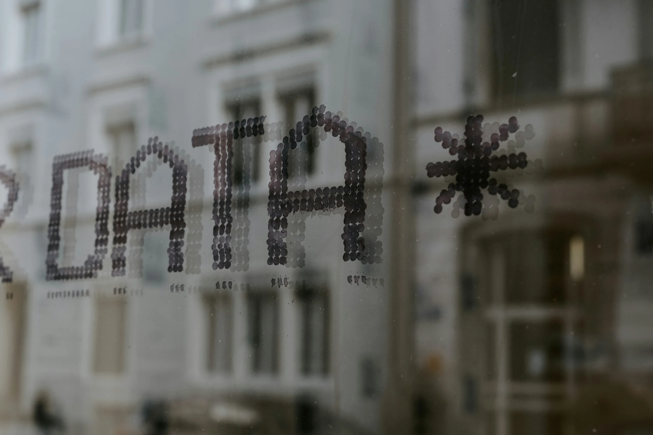 The word DATA and an asterisk symbol are formed by small circular dots on a glass surface, with blurred buildings visible in the background through the window.