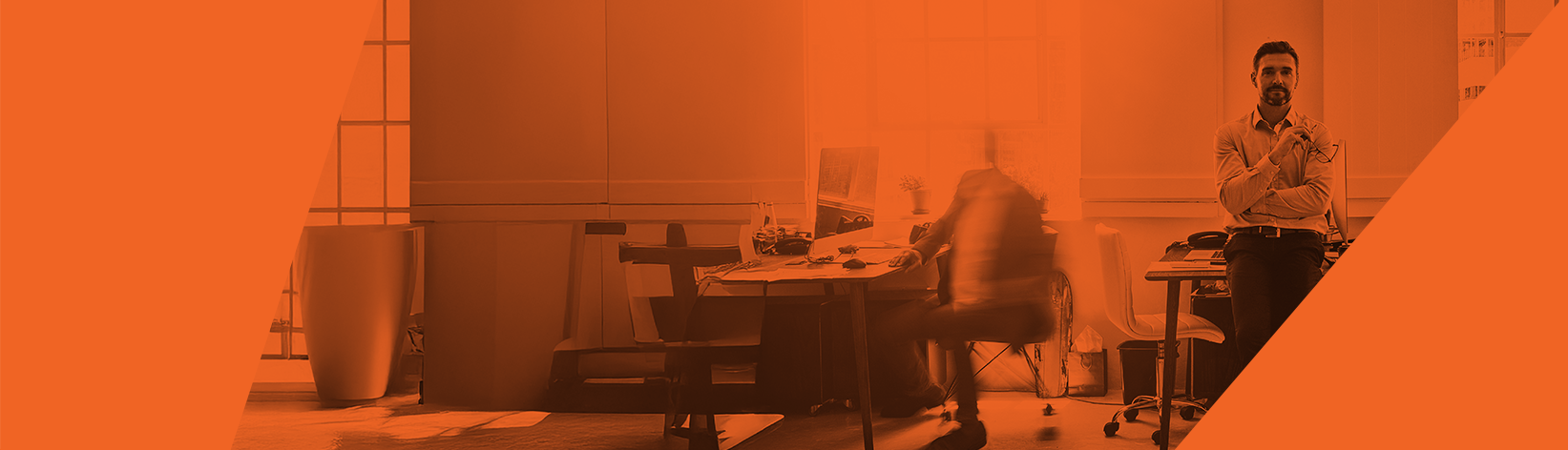 Two people in a modern office with large windows; one sits at a desk with a computer, blurred in motion, while another stands talking on the phone. The image has an orange color overlay.