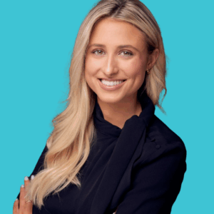 A woman with long blonde hair wearing a black blazer smiles confidently with her arms crossed in front of a bright turquoise background.