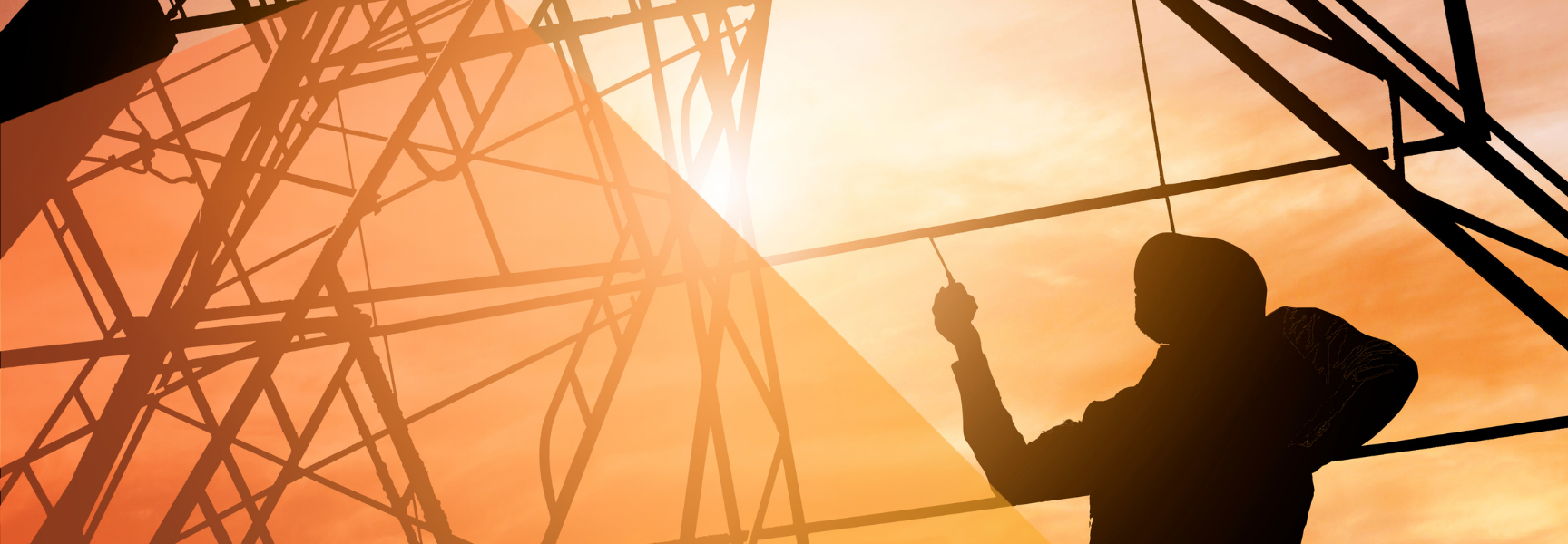 Silhouette of a construction worker holding a tool, standing on scaffolding with a bright orange sunset sky in the background.