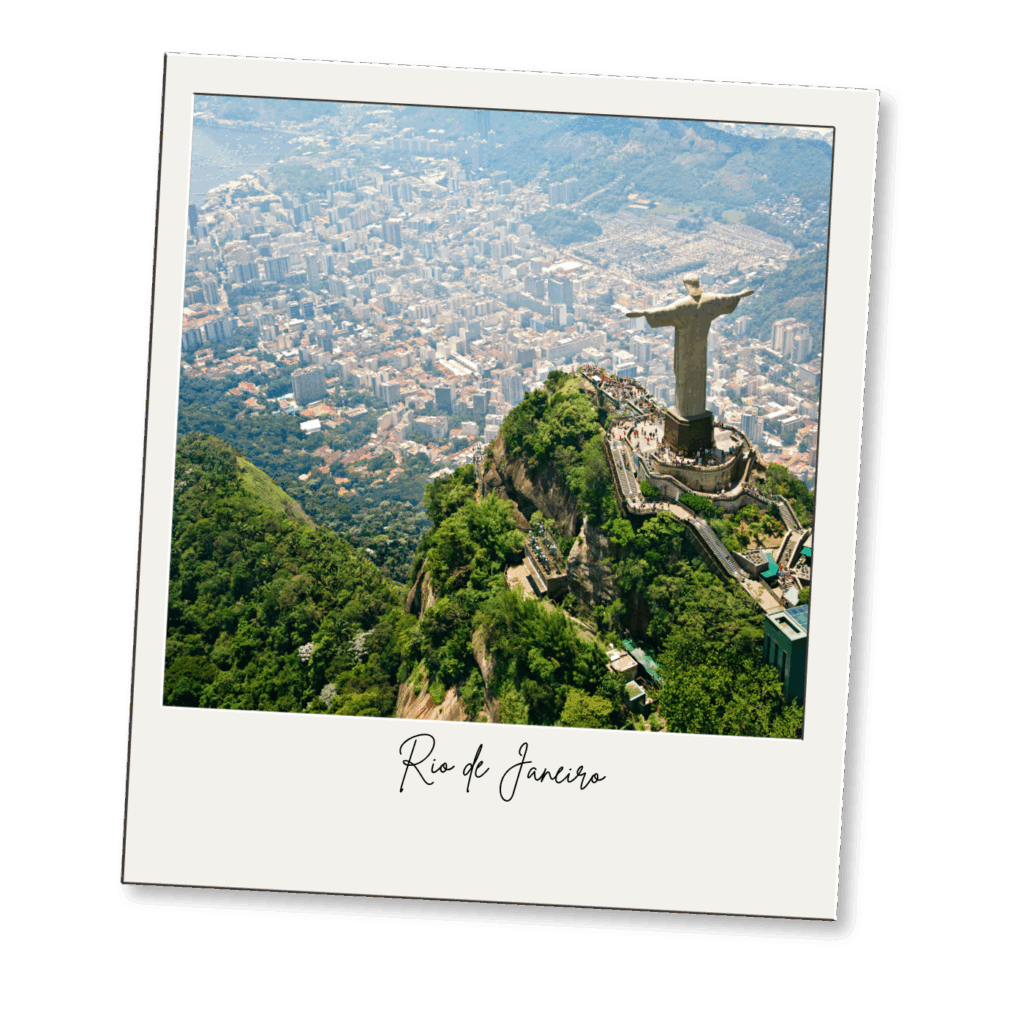Aerial view of Rio de Janeiro with the Christ the Redeemer statue on a hilltop overlooking the city, surrounded by lush greenery and distant buildings.