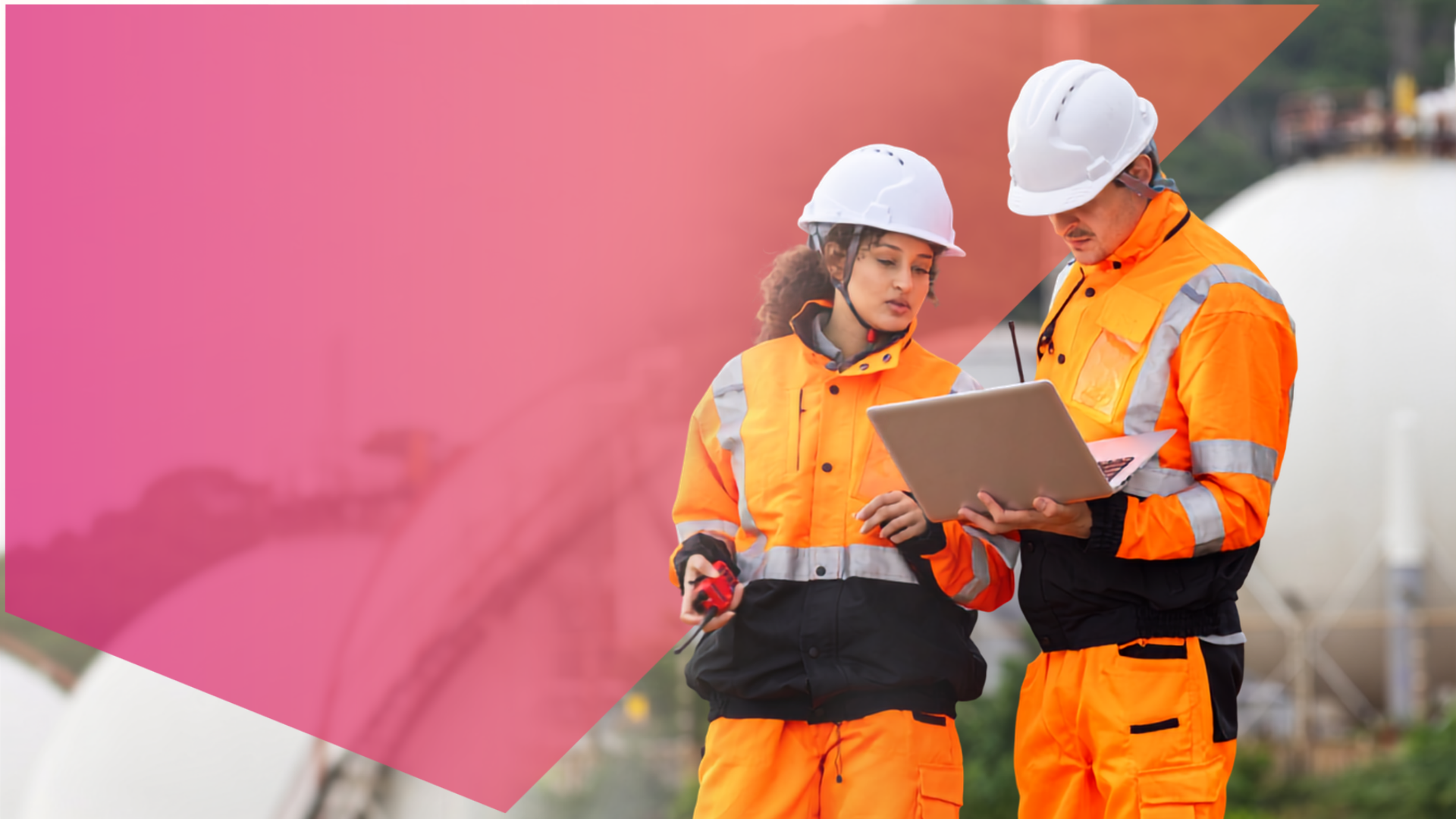 Two workers in orange safety gear and helmets review information on a laptop at an industrial site, with large storage tanks in the background and a pink transparent overlay on the left side.