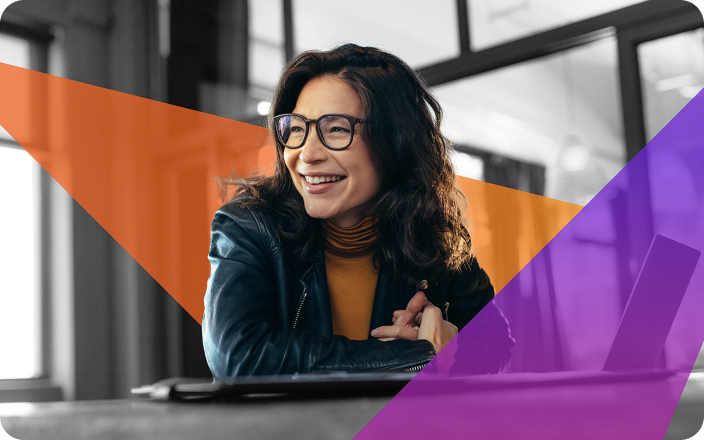 A woman with glasses smiles whilst sitting at a desk, wearing a dark jacket and orange polo neck. The image features orange and purple geometric overlays.
