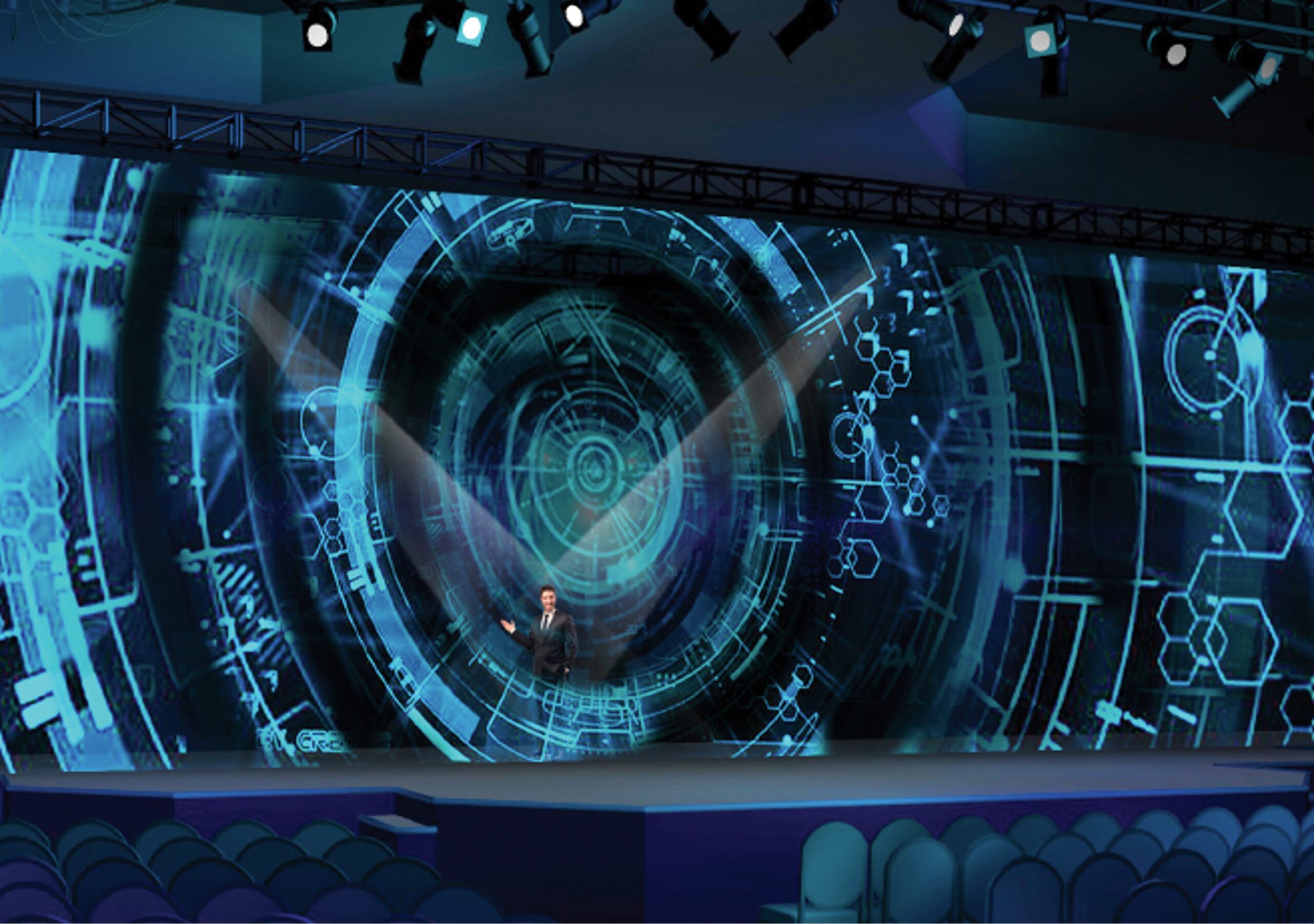 A stage with futuristic blue digital graphics projected on a large screen, displaying circular and hexagonal patterns. A person stands in the center, enhancing the high-tech theme. Rows of empty seats are visible in the foreground.