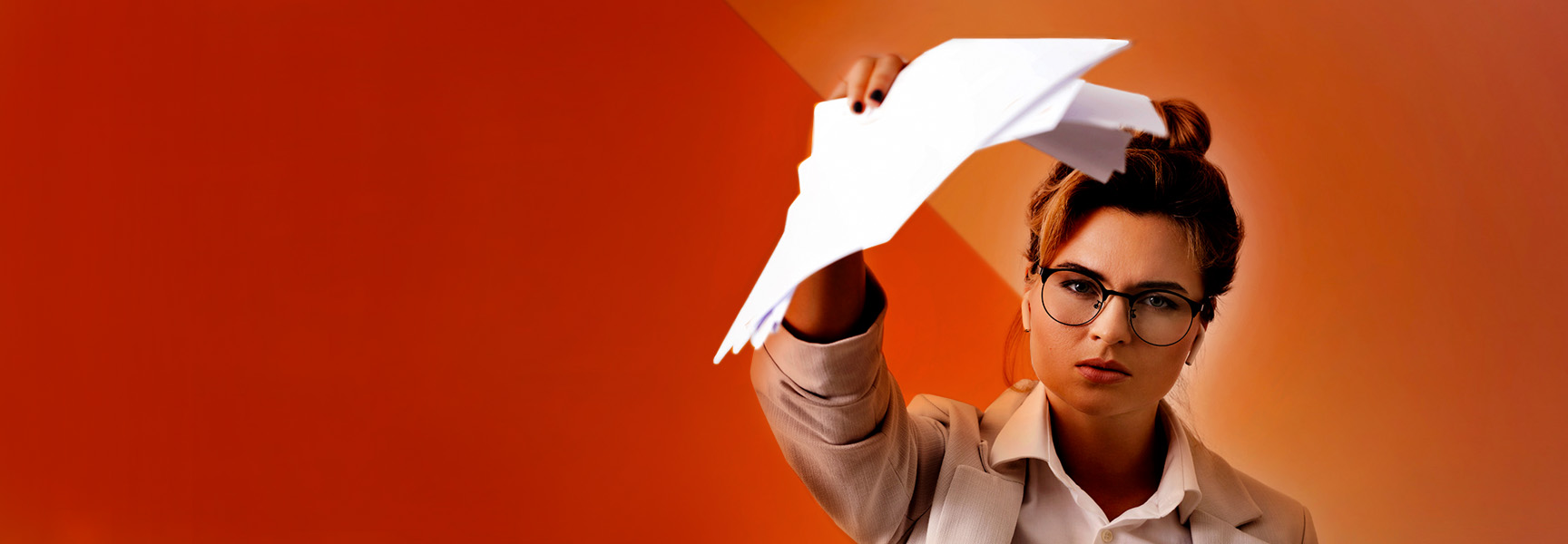 A woman wearing glasses and a beige blazer holds up crumpled papers with a serious expression against an orange geometric background.