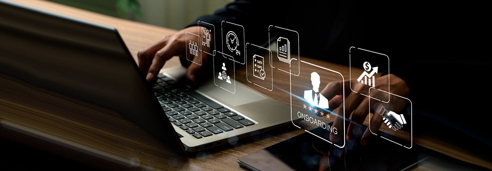 A person typing on a laptop at a desk with virtual icons representing business concepts like data analysis, document management, and collaboration floating above. A tablet also lies on the desk nearby.