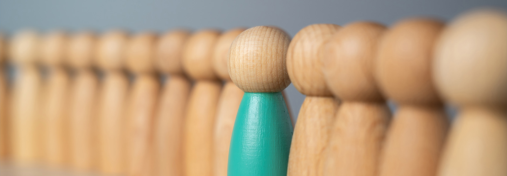A row of wooden peg figures, with one green figure standing out among the natural-colored pegs.