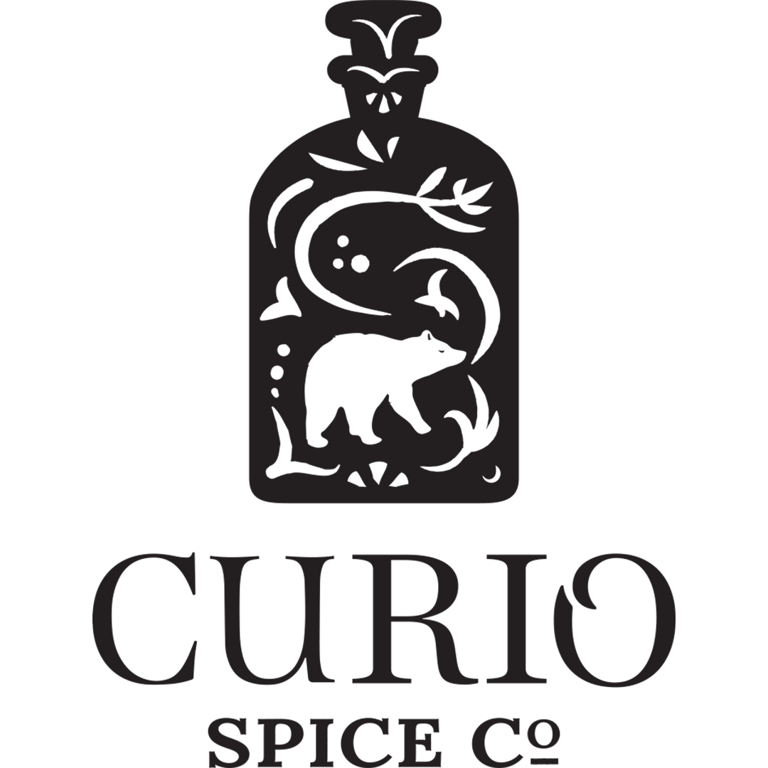A black and white logo features a bottle with a bear, leaves, and stars inside. Below, the text reads CURIO SPICE Co..